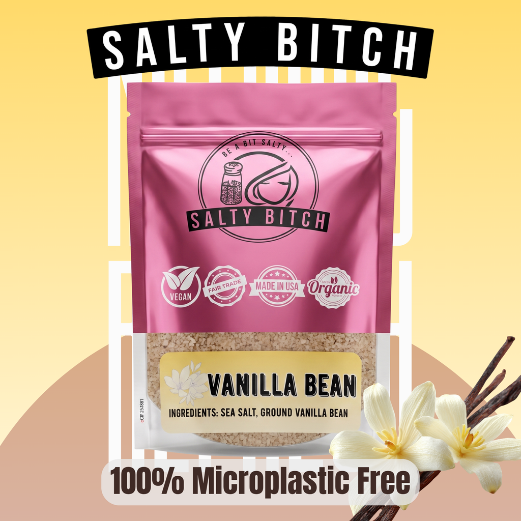 A stand-up pouch of Salty Bitch Vanilla Bean sea salt with a pink upper half and a clear lower half showing the tan vanilla bean powder inside. The pouch has the Salty Bitch logo and icons for vegan, non-GMO, made in USA, and organic.