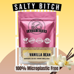 A stand-up pouch of Salty Bitch Vanilla Bean sea salt with a pink upper half and a clear lower half showing the tan vanilla bean powder inside. The pouch has the Salty Bitch logo and icons for vegan, non-GMO, made in USA, and organic.